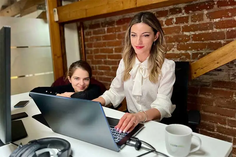 O persoana de marketing și un designer lucrează împreună la birou, cu o cană promoțională Codezilla lângă laptop