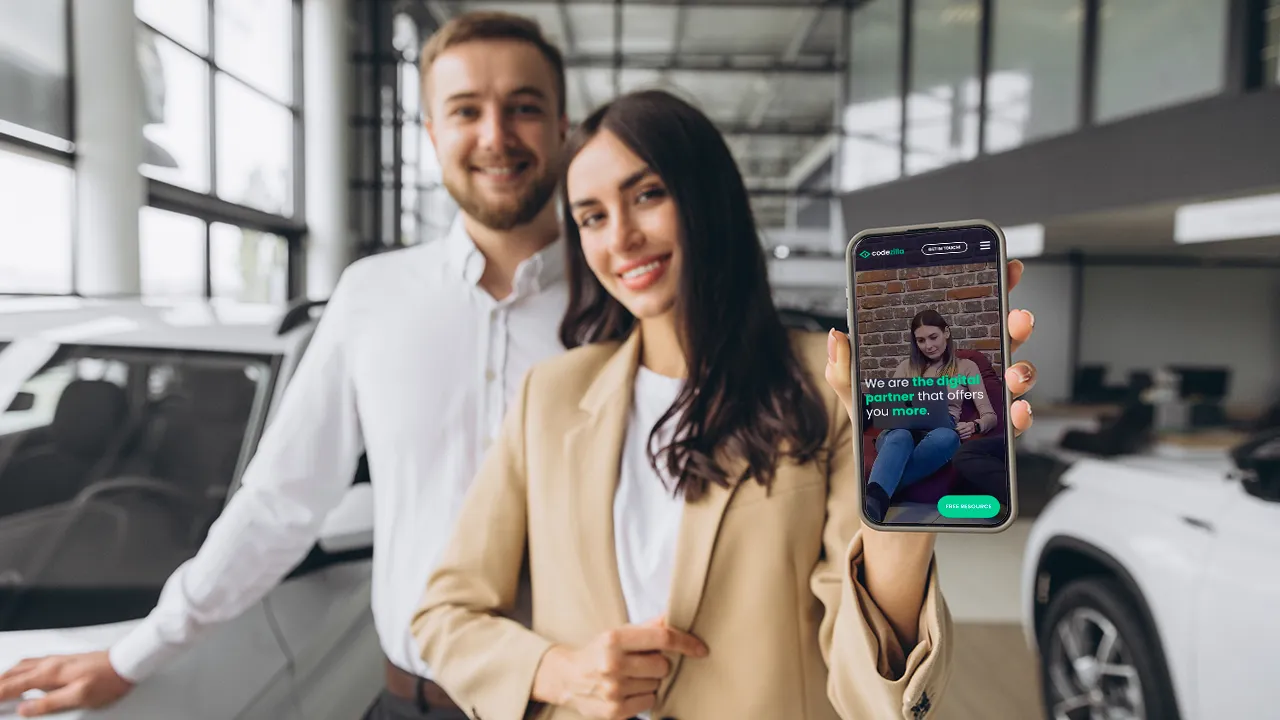 Two professionals in a car dealership, with the woman holding a smartphone displaying the Codezilla website