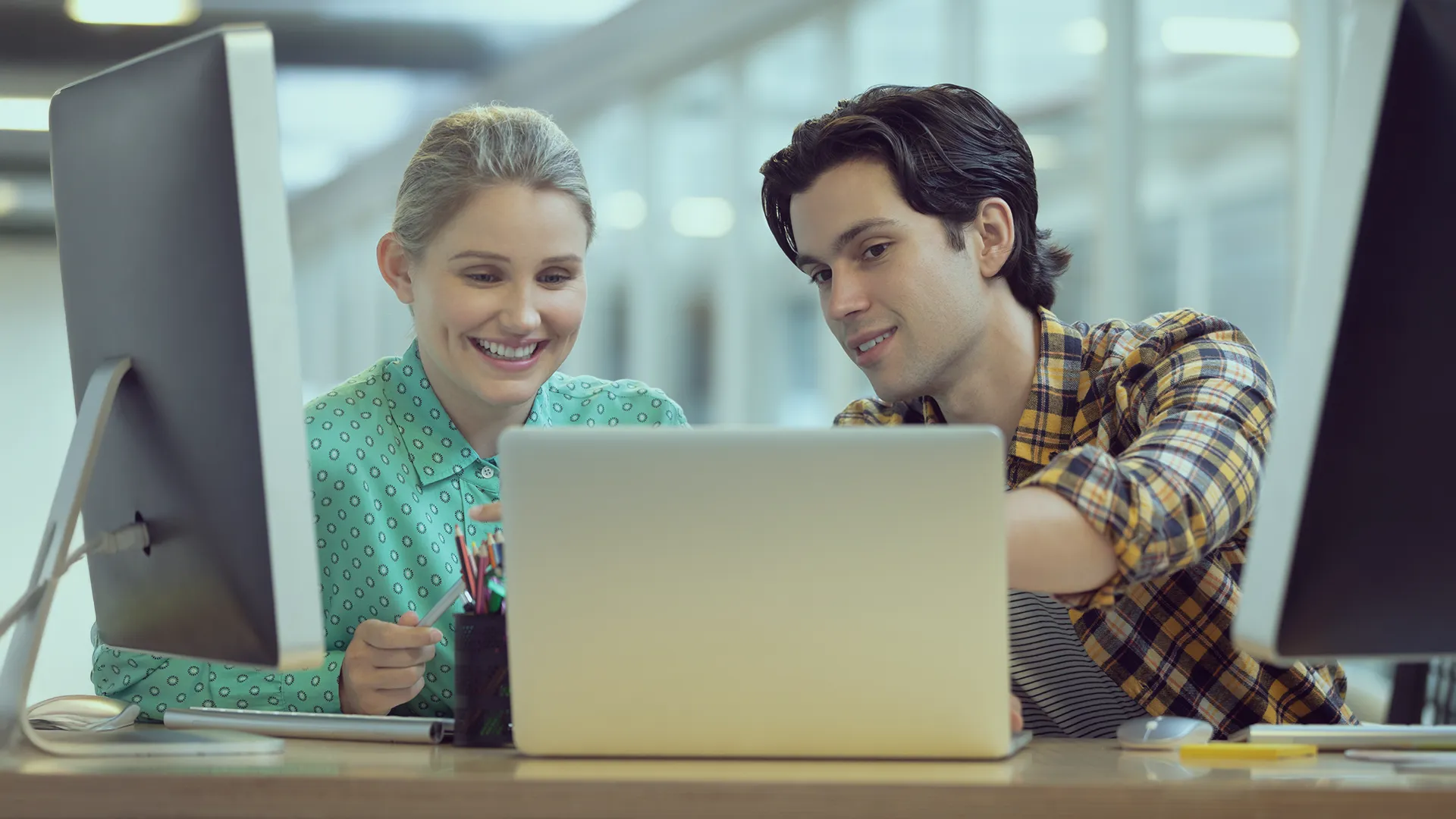 Two team members collaborating at a laptop in a modern office, in a positive and relaxed atmosphere
